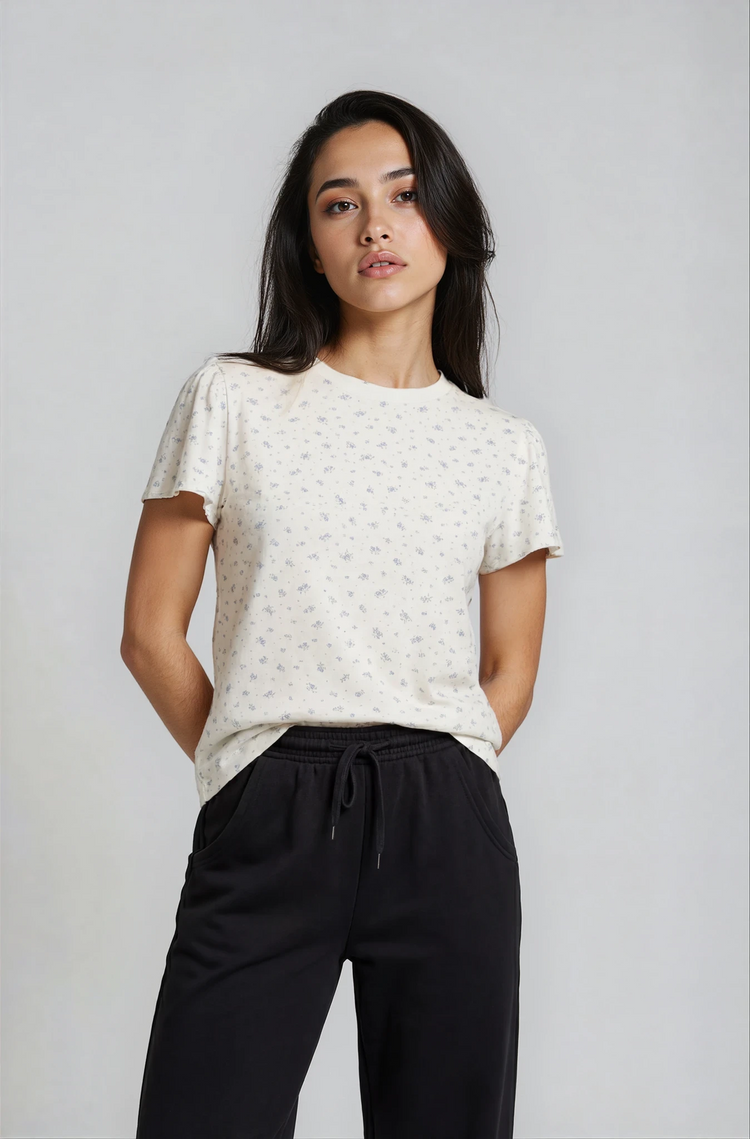 Woman wearing a white patterned top and black pants against a plain background