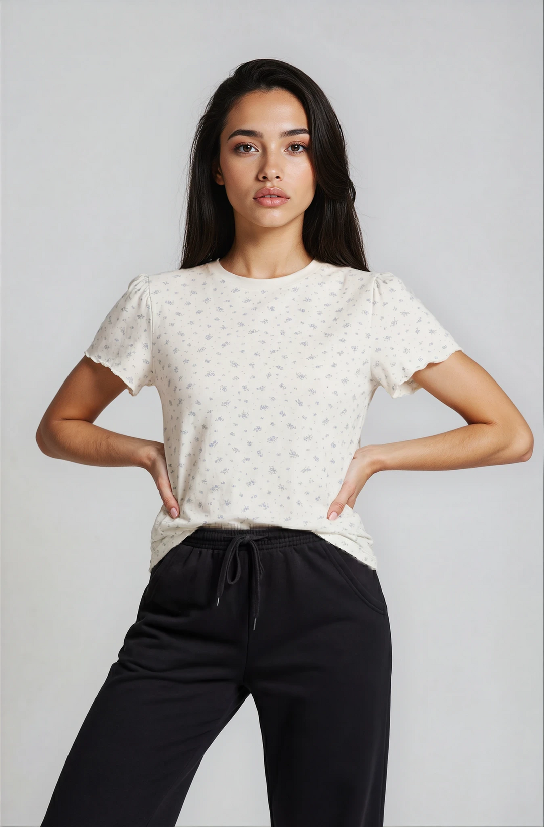 Woman wearing a white floral colette shirt and black pants on a plain background
