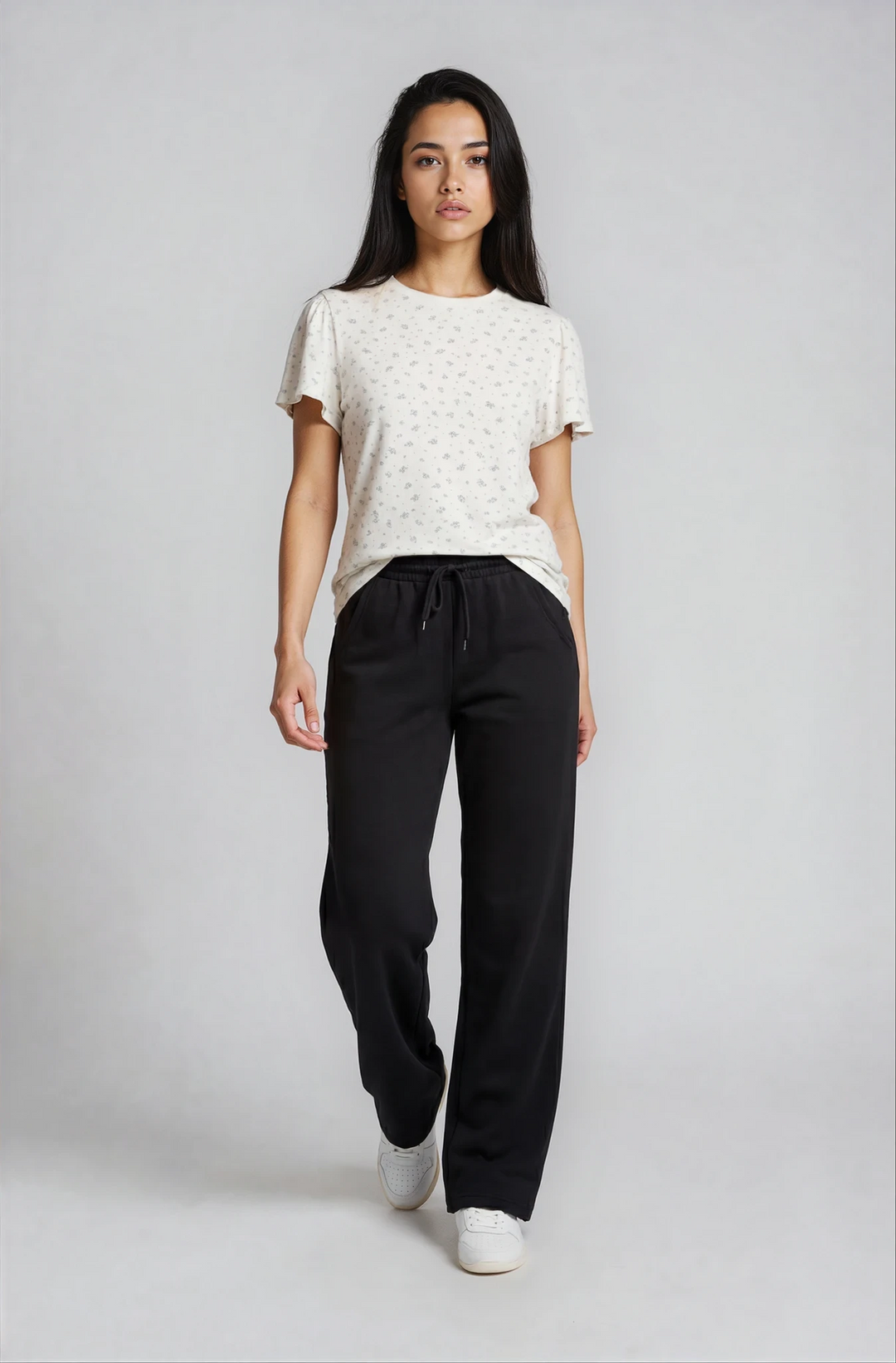 Woman wearing a white top and black adora luxe flow pants on a plain background