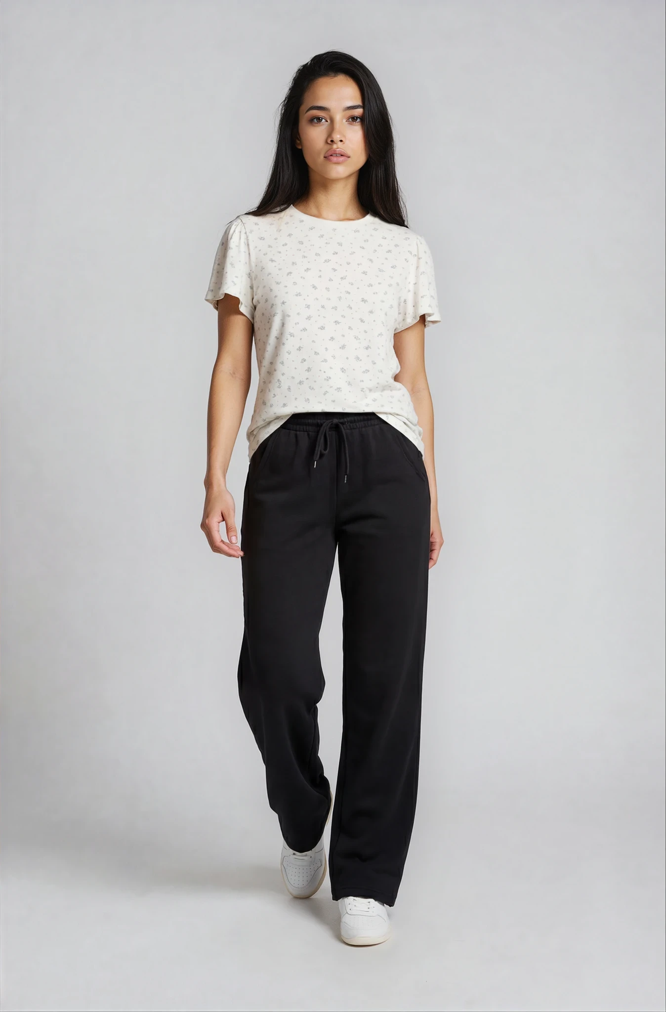 Woman wearing a white top and black adora luxe flow pants on a plain background