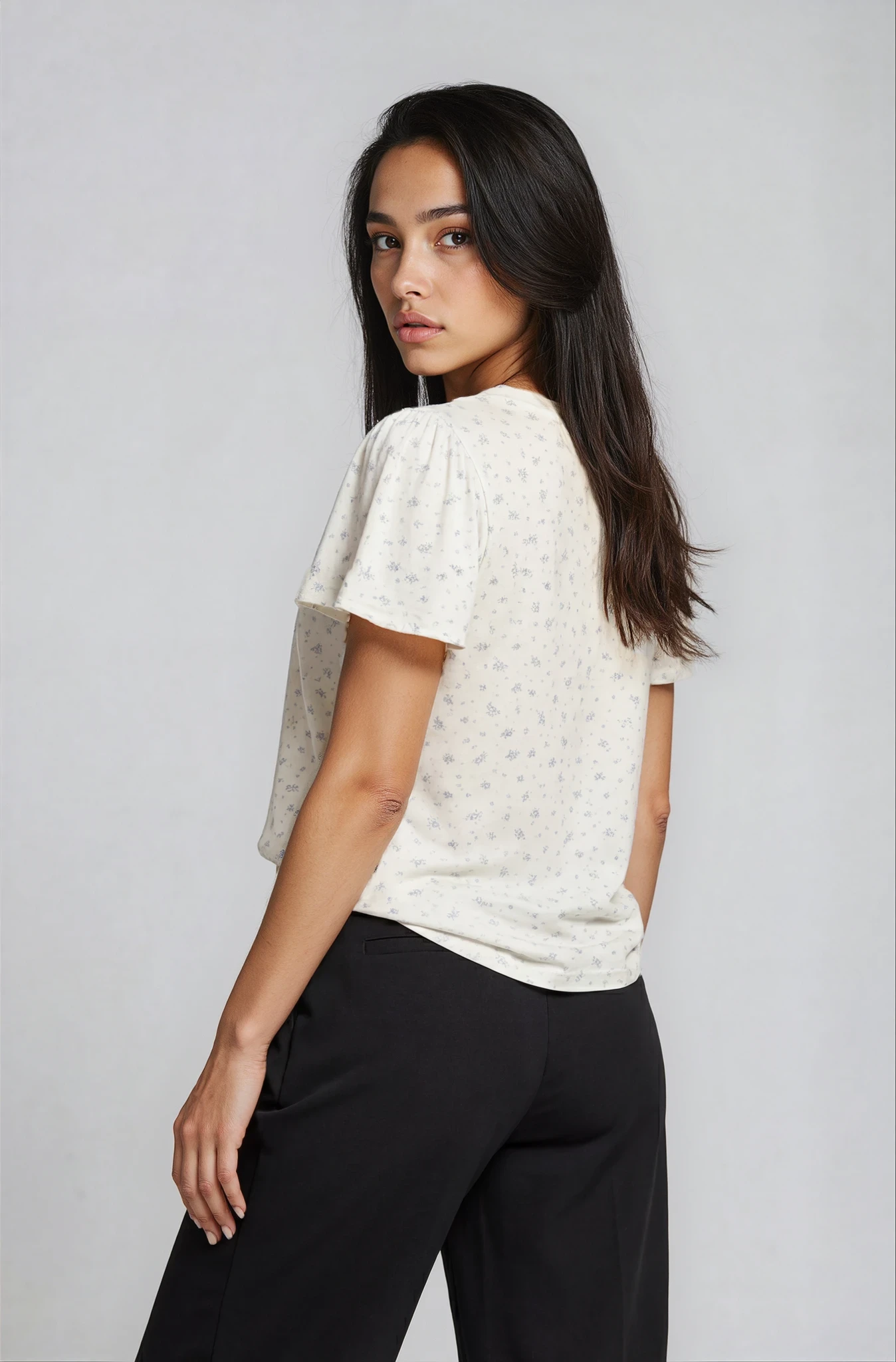 Woman wearing a white blouse with short sleeves and black pants on a plain background