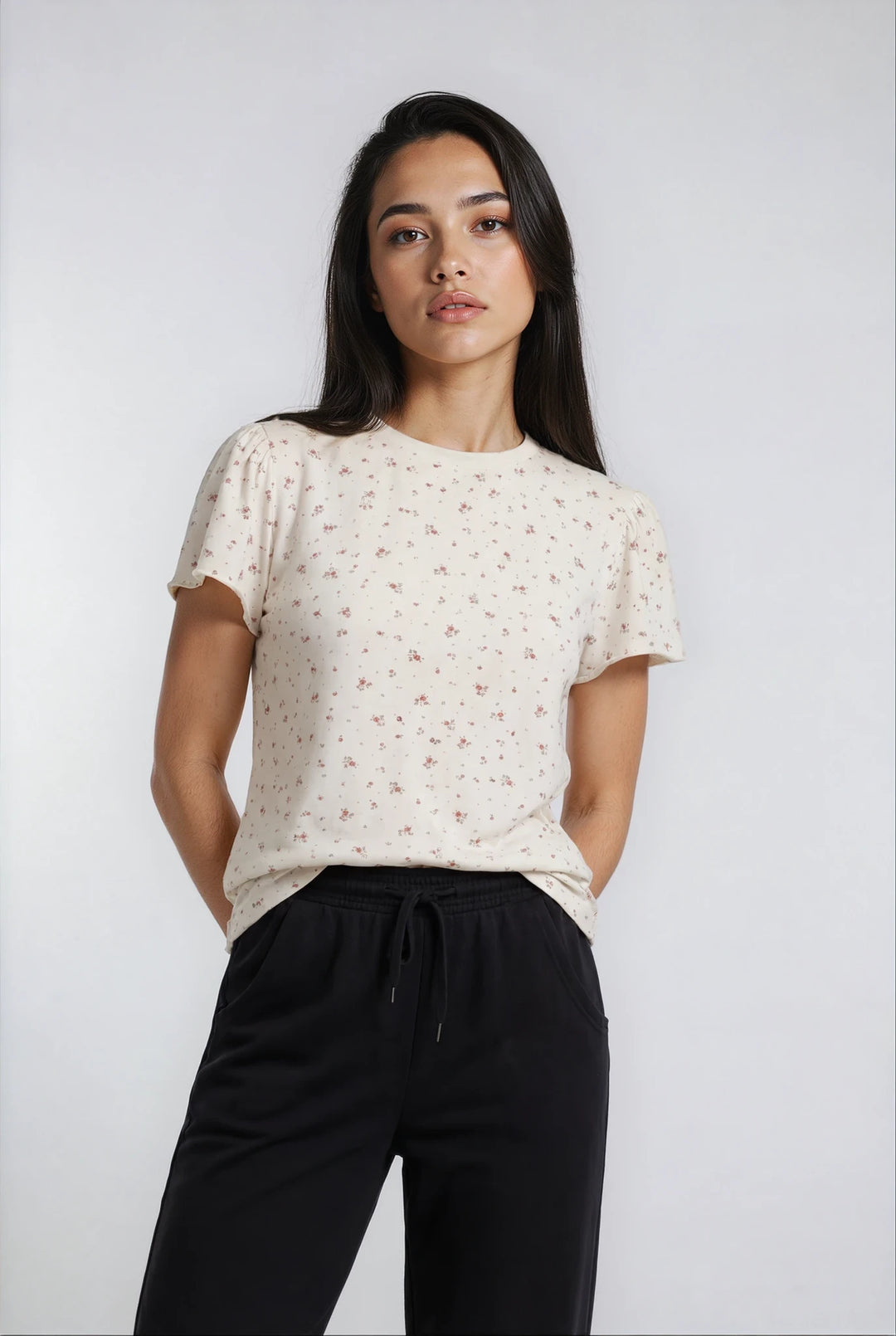 Woman wearing a white floral blouse and black luxe flow pants against a plain background