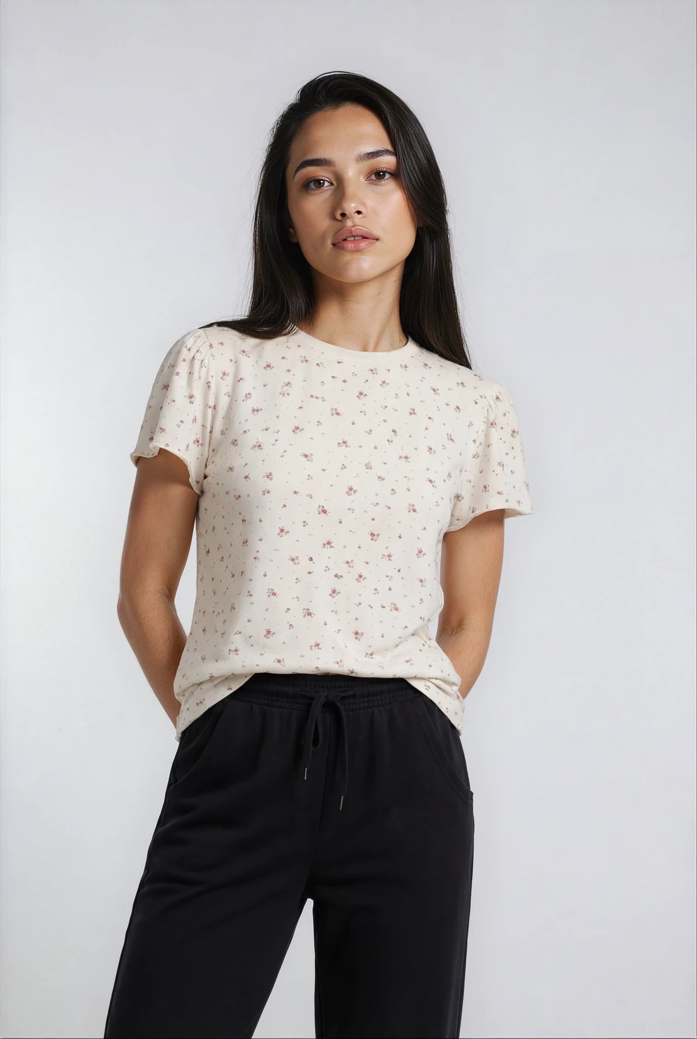 Woman wearing a white floral blouse and black luxe flow pants against a plain background