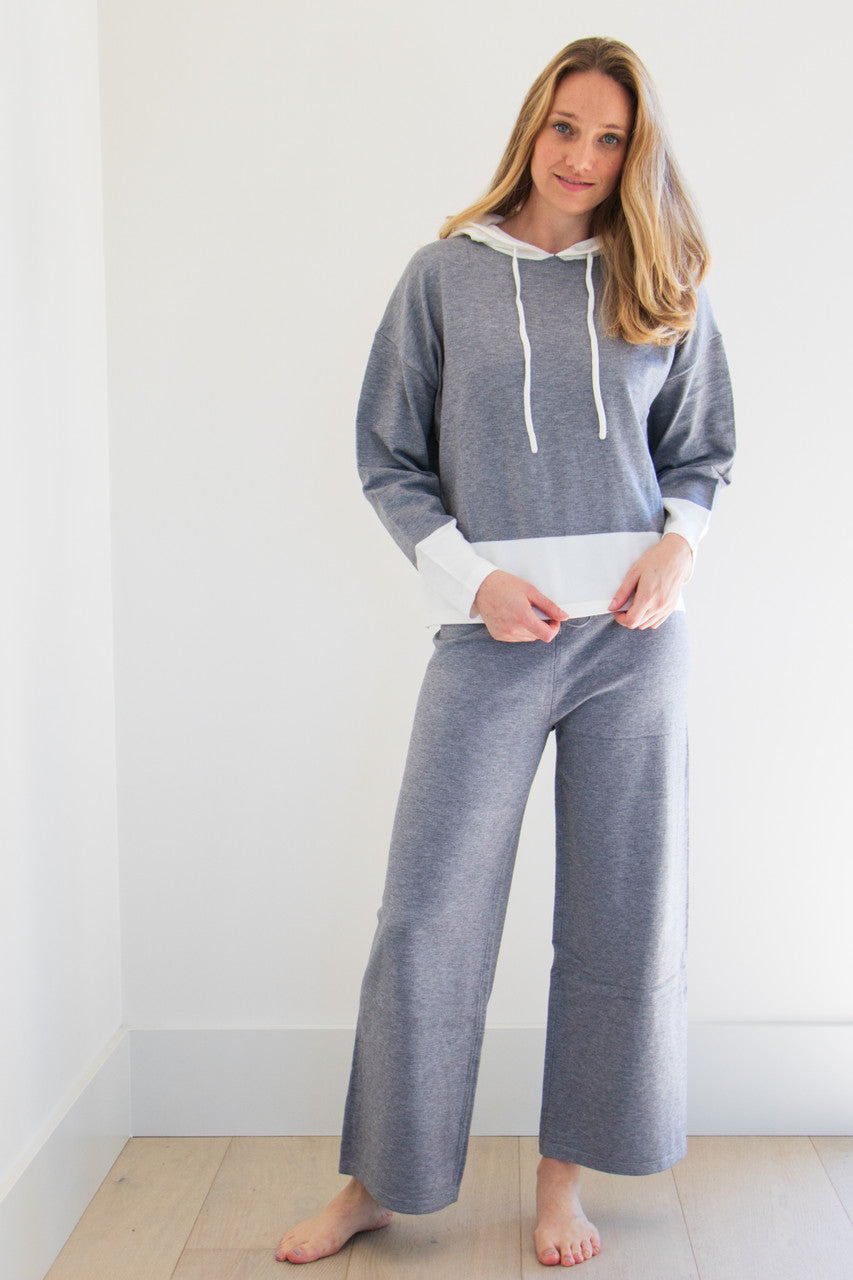 A two piece set in heather grey fabric with bold, colour blocked white accents. The hooded boxy fitted top is paired with a slightly cropped wide leg gaucho trouser, made for lounging in comfort. 

