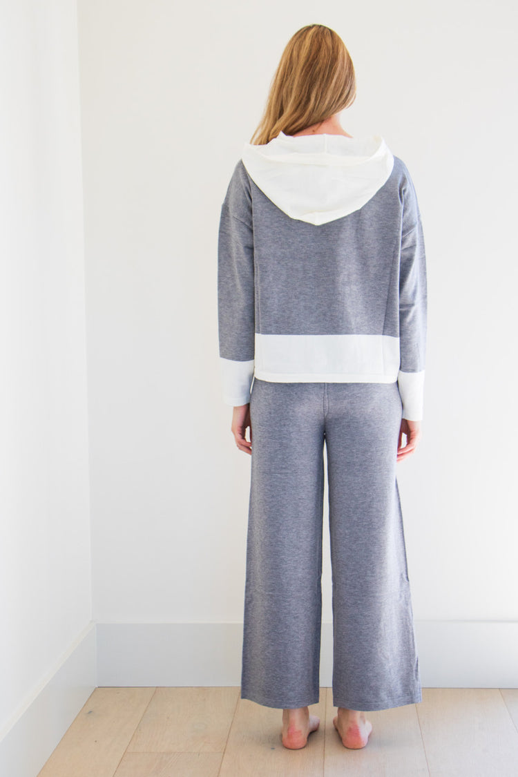 A two piece set in heather grey fabric with bold, colour blocked white accents. The hooded boxy fitted top is paired with a slightly cropped wide leg gaucho trouser, made for lounging in comfort. 

