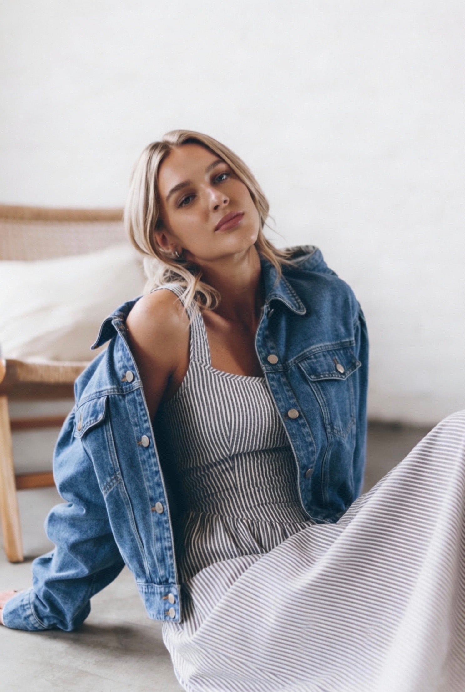 Woman wearing a denim jacket and priv Jules striped dress sitting on a couch.